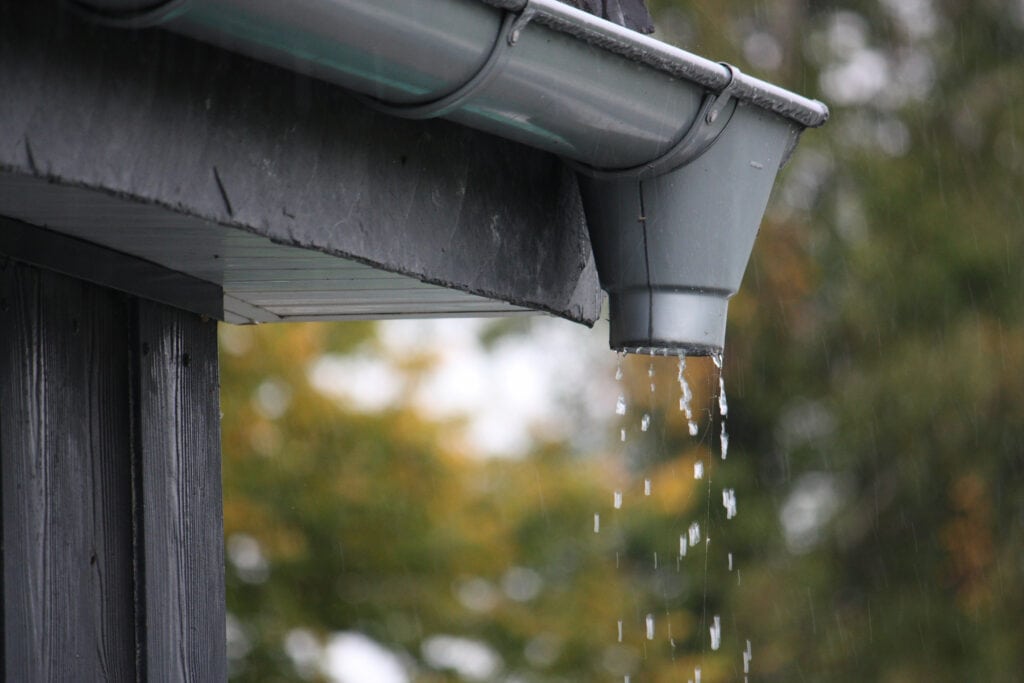 a rain gutter drips from the roof of a house.